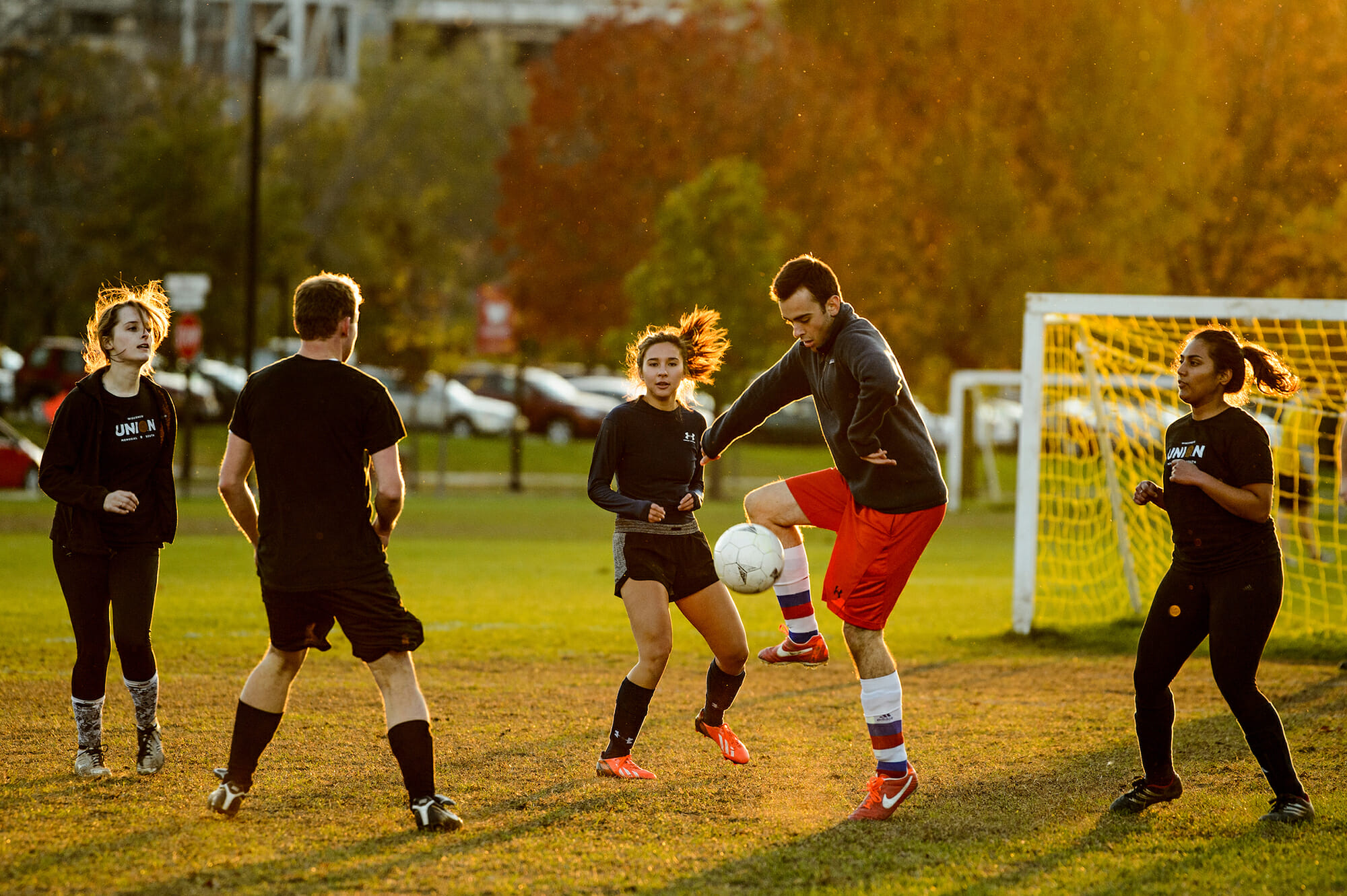 Under a setting sun, students play soccer on a field outside of DeJope residence hall
