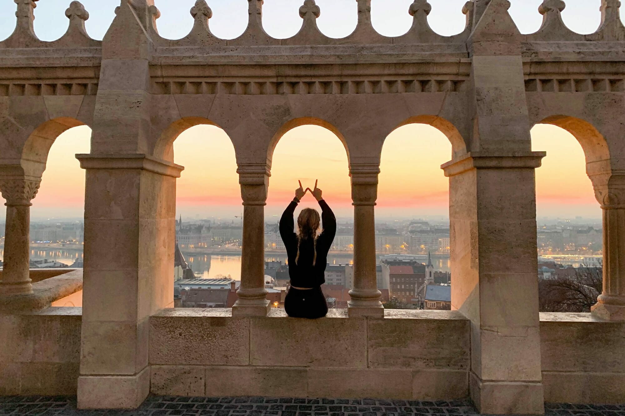 Student silhouette on an ornate building in a foreign country showing the W sign with hands